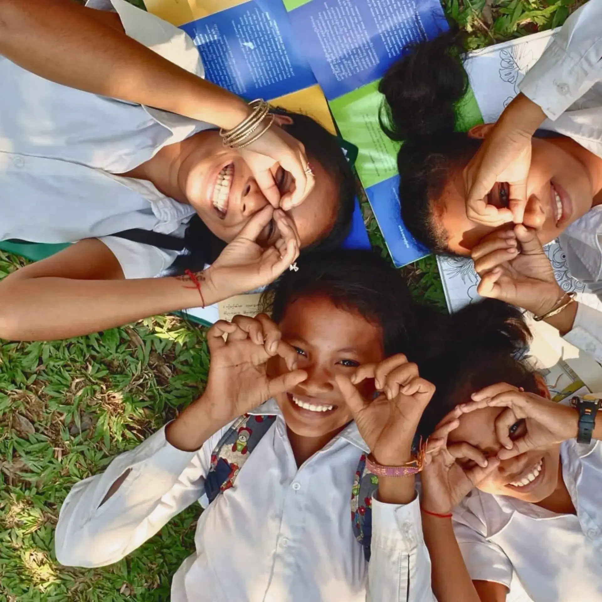 Four smiling children making circles around their eyes with their hands